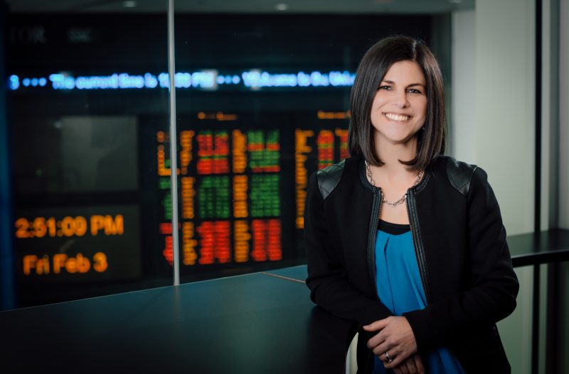 Online FinTech Master's Degree student smiling in front of financial analysis report screens. 
